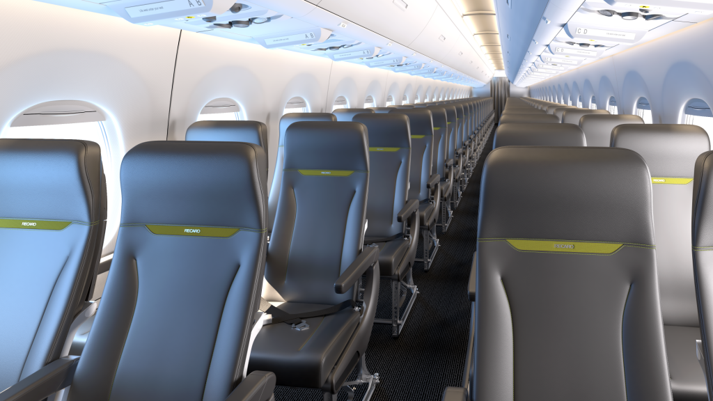 The image shows the interior of an airplane cabin, specifically the economy class section. The seats are arranged in rows, with three seats on each side of the aisle. The seats are upholstered in dark gray material with green accents and have the brand name "RECARO" on them. The cabin is well-lit, and the overhead compartments are closed. The windows along the sides of the cabin are visible, allowing natural light to enter. The overall appearance is clean and modern.