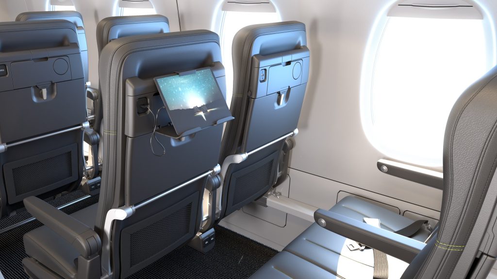 The image shows the interior of an airplane cabin, specifically the economy class seating area. The focus is on the back of two rows of seats. Each seat has a built-in entertainment screen, and one of the screens is displaying an image. The seats are upholstered in dark material, and there are tray tables folded up on the back of each seat. The cabin is well-lit, with light coming in from the windows on the right side of the image. The floor is carpeted, and there are armrests and seatbelt buckles visible on the seats.