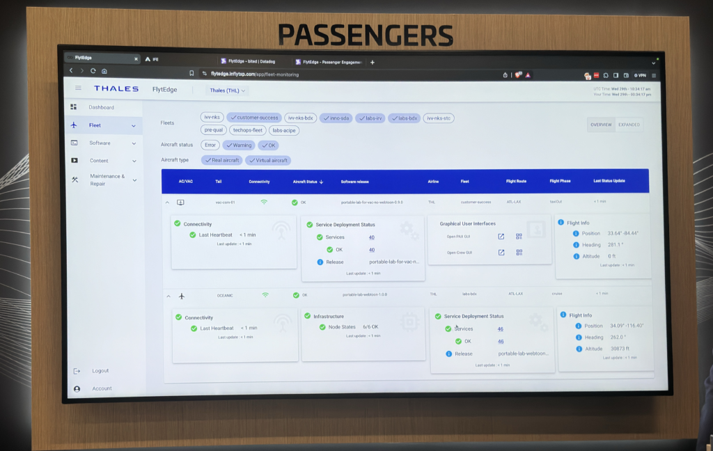 Alt text: A large screen displays a software interface for monitoring aircraft status. The interface includes sections for fleet management, software, content, and maintenance & repair. The main section shows detailed information about aircraft connectivity, service deployment status, graphical user interfaces, and flight information such as position, heading, and altitude. The screen is labeled "PASSENGERS" at the top. The software appears to be from Thales and is named FlytEdge. Various filters and status indicators are visible, including connectivity status and last heartbeat updates.